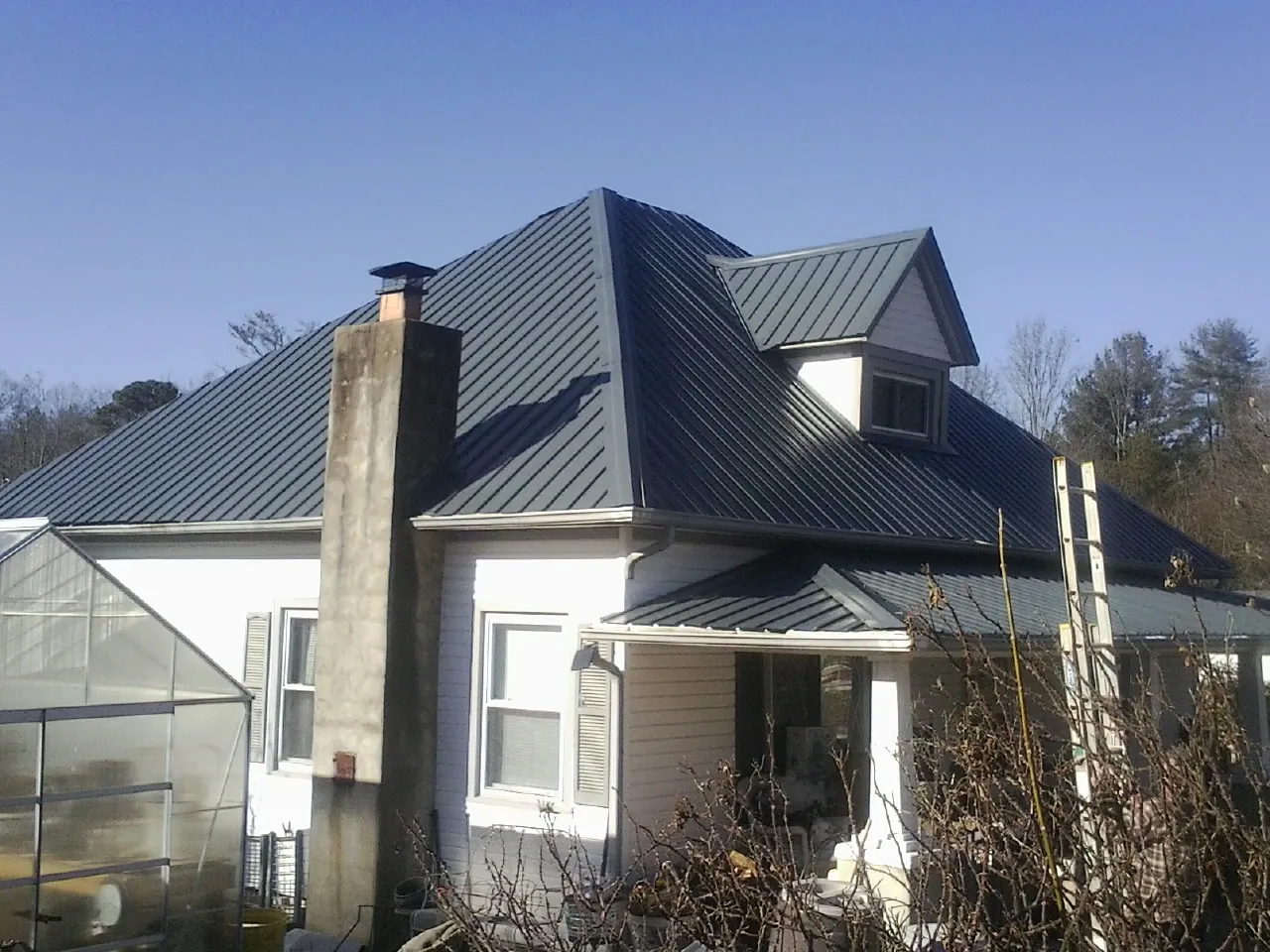 Dark blue standing seam metal roof on a white farmhouse with dormer — Slate & Tile Roof Repair by Roofing Brothers in Baltic