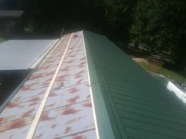 Old rusted panels beside newly installed green metal roofing — Wind Damage Roof Repair by Roofing Brothers in Baltic